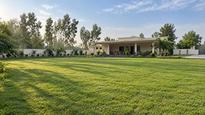 Large green farmhouse lawn with trees and a single-storey house behind it